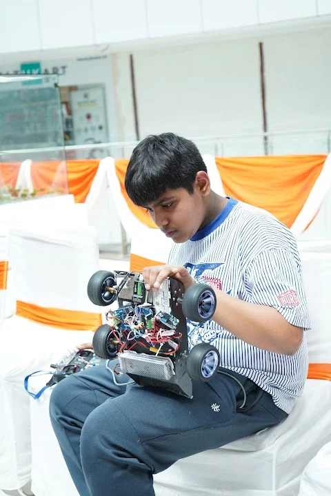 Young RGI 2026 participant checking the exposed electronics and wheels of his robot before play