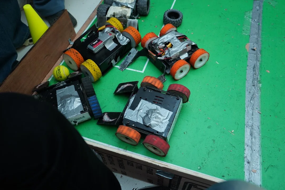 Student-built soccer robots with coloured wheels on the RGI 2026 pitch