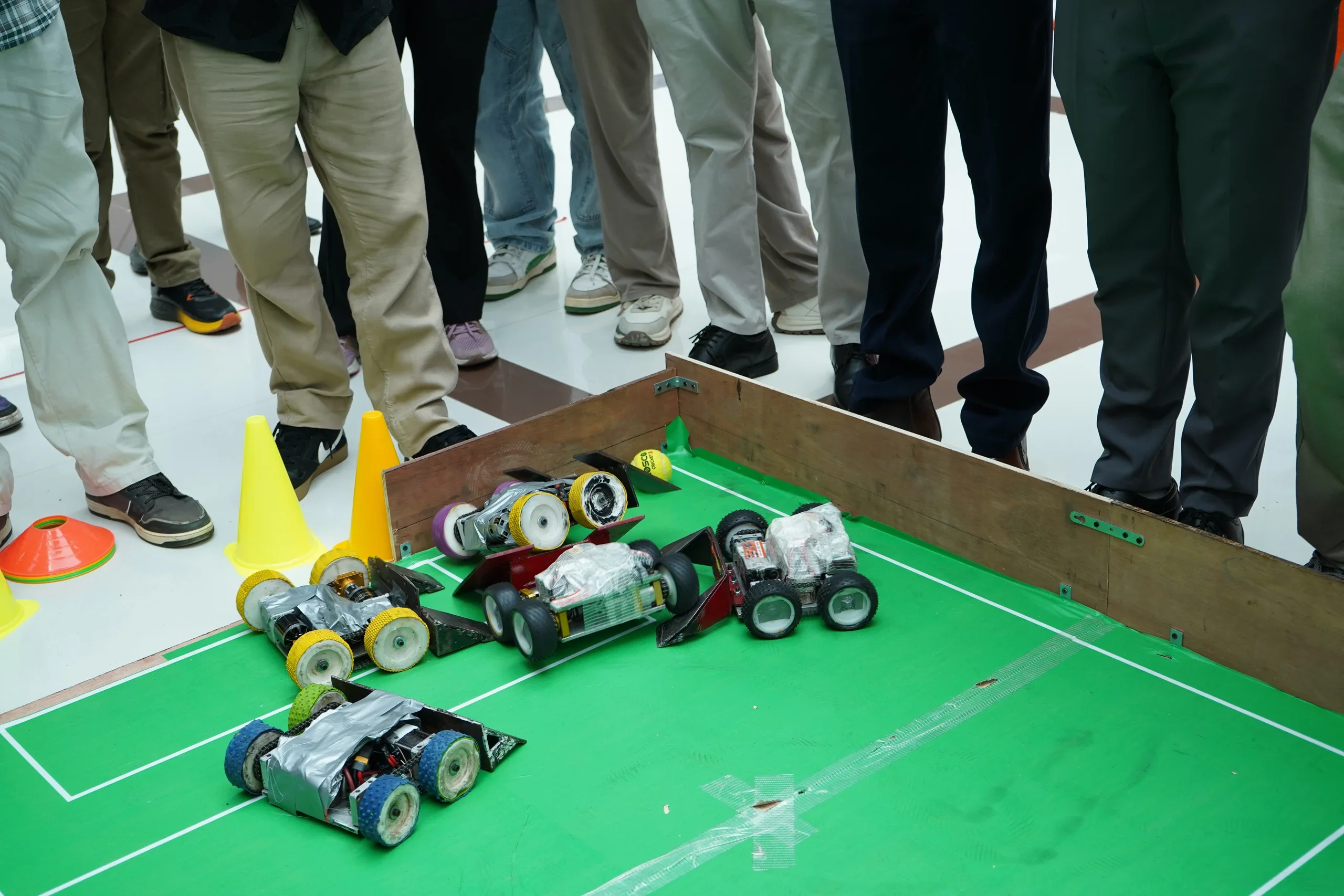 Custom robots with colourful wheels gathered near the RGI goal